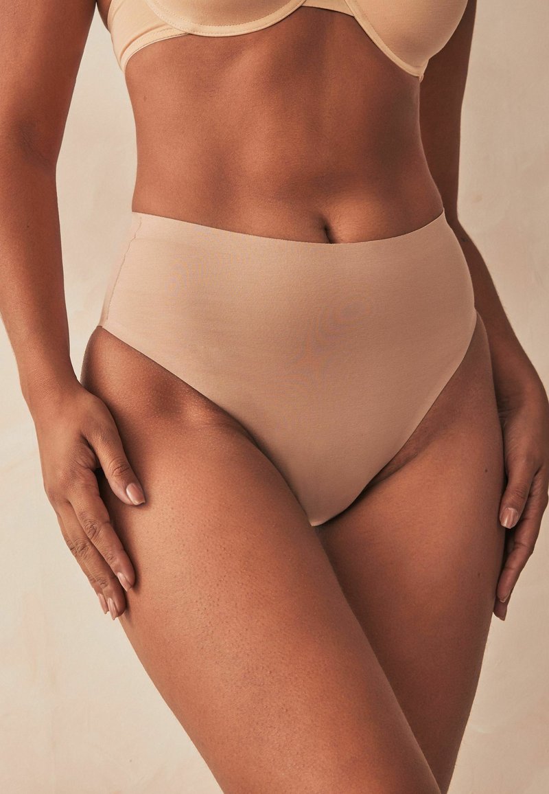 Hooggesneden slip in beige stof, gladde textuur, elastische band, ontworpen voor comfort met een naadloze afwerking en volledige dekking.