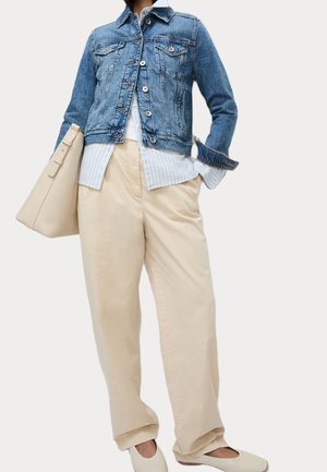 Persoon die een blauwe spijkerjas draagt over een gestreept overhemd, beige wijde broek, witte platte schoenen en een grote beige handtas draagt.