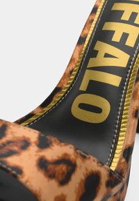 Sandalias de tacón alto con estampado de leopardo y punta abierta, con un forro interior negro y un logo de marca dorado en la parte delantera. Material texturizado.