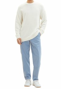 Sweter w kolorze kremowym, teksturowany, z okrągłym dekoltem, w zestawie z jasnoniebieskimi, luźnymi spodniami. Całość uzupełniona białymi trampkami.