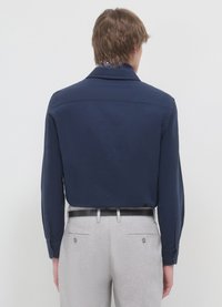 Marineblaues, langärmliges Hemd mit Kragen und Rückenteil. Kombiniert mit hellgrauen Hosen und einem schwarzen Gürtel. Glatte Stoffstruktur.