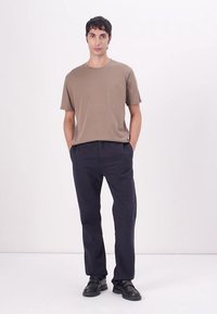 Beige bavlněné tričko a tmavě modré kalhoty, nošené s černými skládacími botami. Tričko má kulatý výstřih a krátké rukávy.