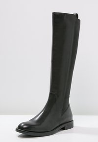 Bota de cuero negra hasta la rodilla con tacón bajo y panel elástico en la parte trasera para un ajuste ajustable.