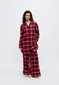Σετ πυτζάμες φανέλας με κόκκινο και μαύρο καρό σχέδιο, που περιλαμβάνει μακρυμάνικο πουκάμισο με κουμπιά και παντελόνι με φαρδιές παντελόνες, με λογότυπο στο στήθος και απαλή υφή.