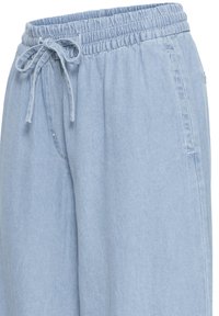 Pantalon à taille élastique bleu clair avec cordon de serrage et poches latérales, présentant une texture de tissu douce et lisse ainsi qu'une coupe décontractée.