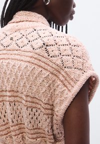 Ανοιχτό ροζ πλεκτό πουλόβερ με ανοιχτά σχέδια πλέξης, οριζόντιες ρίγες και διακριτικά παγέτες. Διαθέτει άνετη εφαρμογή και κοντά μανίκια.