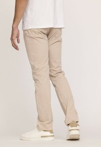 Pantalons slim beige en tissu doux, avec un design épuré, une coupe droite et des poches arrière cousues, associés à des baskets blanches.