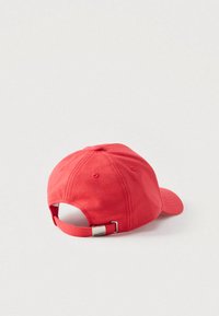 Boné de basebol vermelho ajustável com fecho de fivela metálica, detalhes de costura e ilhós de ventilação num fundo branco liso.