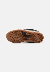 Suola di sneakers nera e marrone con una presa in gomma testurizzata, caratterizzata da un motivo geometrico e un logo nero evidente.