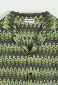 Chemise à manches courtes avec un motif en zigzag présentant des couleurs vertes, bleues et brunes. Fabriquée à partir d'un tissu léger et texturé avec un col.