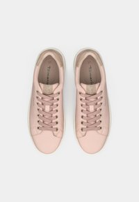 Une paire de baskets à lacets rose pâle avec des accents métalliques au niveau du talon et de la languette, vues de dessus sur un fond blanc.