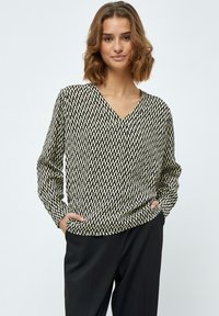 Langärmlige Bluse mit V-Ausschnitt in einem schwarz-weißen geometrischen Muster, mit lockerer Passform und seitlichen Taschen. Hergestellt aus einem glatten, leichten Stoff.
