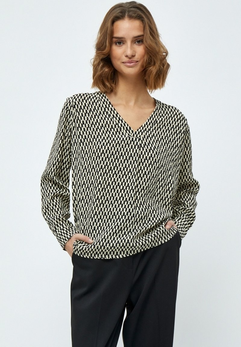 Langärmlige Bluse mit V-Ausschnitt in einem schwarz-weißen geometrischen Muster, mit lockerer Passform und seitlichen Taschen. Hergestellt aus einem glatten, leichten Stoff.