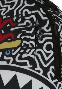 Mochila de diseño en blanco y negro con vibrantes acentos en rojo, amarillo y azul, fabricada con un material duradero y un compartimento con cremallera.