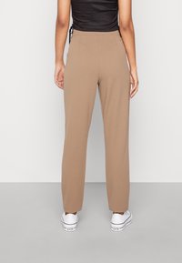 Brązowe dopasowane spodnie o gładkiej teksturze, prostym kroju nogawki, średnim stanie i z tylnymi kieszeniami, w połączeniu z białymi trampkami.