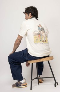 Kreminė medvilninė marškinė su retro teniso grafika ant nugaros. Modelis vilki tamsiai mėlynus džinsus ir pilkus sportbačius su akcentais.