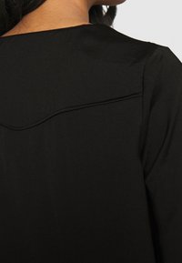 Maglietta nera con scollatura tonda, tessuto texturizzato e un sottile dettaglio cucito lungo la cucitura posteriore, tessuto morbido.