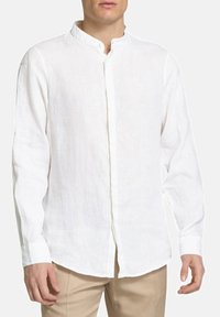 Camicia bianca in lino a maniche lunghe con colletto alto, chiusura frontale con bottoni e taglio dritto. Presenta una leggera texture e maniche con polsini.