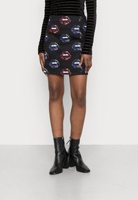 Svart minikjol med färgglada läpptryck, parat med svarta klackade ankelstövlar och en långärmad topp med svarta ränder.