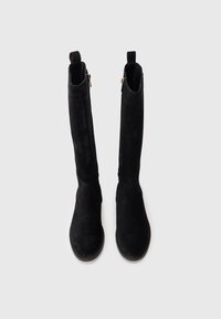 Bottes noires en daim jusqu'au genou avec une texture lisse, bout rond et accents en zip doré à l'arrière, dotées de poignées à l'axe.