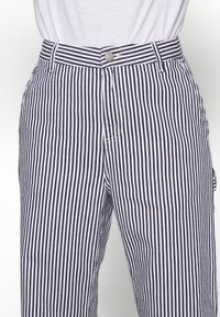 Granatowo-białe spodnie w paski o prostym kroju, z zapięciem na guziki i szlufkami na pasek, wykonane z lekkiego materiału.