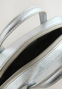 Srebrna metaliczna torebka z teksturowanej skóry, z podwójnymi zapięciami na zamek i krótkimi uchwytami, odsłaniająca czarne wnętrze.