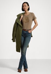 Brun t-shirt med präglad design, grön trenchcoat, blå jeans och bruna klackboots. Looken kompletteras av ett brunt bälte.