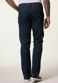 Jeans in denim blu scuro con design a cinque tasche, dettagli di cucitura visibili e gamba dritta, indossati con sneakers nere.