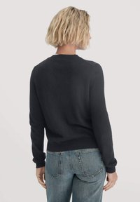 Schwarzer Pullover mit rundem Halsausschnitt und langen Ärmeln, gefertigt aus einem weichen Material. Kombiniert mit blauen Jeans, die ein schlichtes Design zeigen.