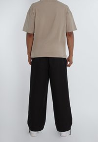 Camiseta beige de manga corta y pantalones negros holgados. La camiseta tiene un cuello redondo, y los pantalones cuentan con cremalleras en los tobillos.