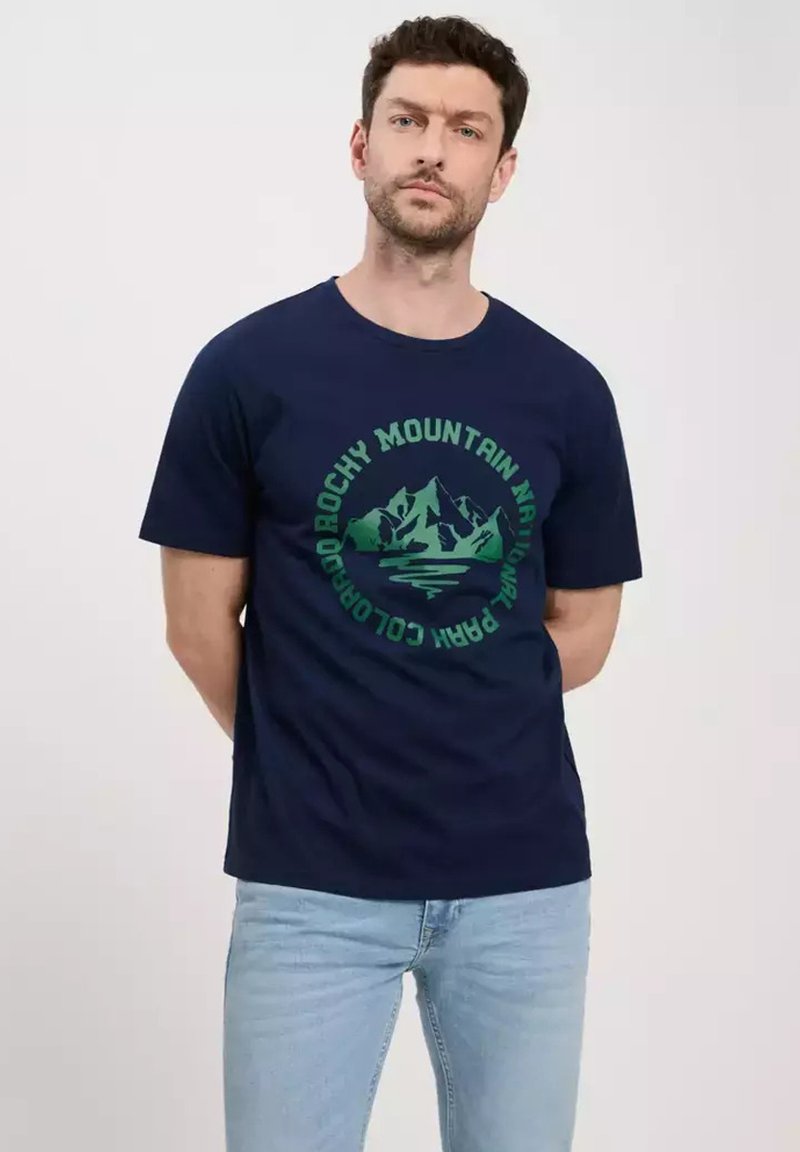 Granatowa bawełniana koszulka z krótkim rękawem z zielonym graficznym wzorem góry oraz tekstem w okrągłym układzie. Klasyczny krój i okrągły dekolt.