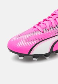 Scarpino da calcio rosa con superiore sintetico testurizzato, presenta accenti neri e bianchi e motivi a strisce diagonali sulla punta.