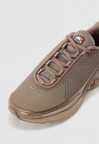 Brown mesh athletic shoe featuring a patterned design, rounded toe, lace-up front, and a visible air unit in the sole.