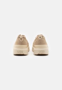Beige Wildleder-Sneaker mit strukturierter Oberfläche, ausgestattet mit einer klobigen cremefarbenen Sohle und dezenter Markenkennzeichnung an der Ferse.