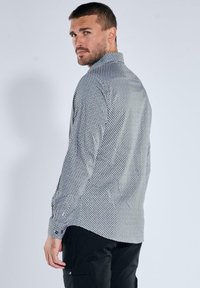 Musterhemd mit langen Ärmeln in Schwarz und Weiß mit geometrischem Design, Kragen und Knopfmanschetten. Der Stoff hat eine glatte Textur.