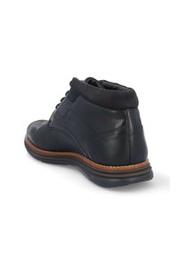 Botín negro de cuero con acabado liso, puntera redondeada y suela de goma color marrón. Presenta costuras en contraste y un collarín acolchado.