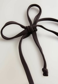 Bandeau en tissu brun foncé avec un nœud central et des boucles étendues de chaque côté, posé sur une surface claire.