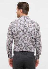 Langarmshirt met een witte basis en een donker bloem- en bladenpatroon. Gekraagde uitvoering met knoopmanchetten, gecombineerd met donkere broek.
