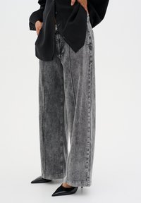 High-waisted, wide-leg gray denim jeans with a faded texture, complemented by a black blouse and pointed black heels.