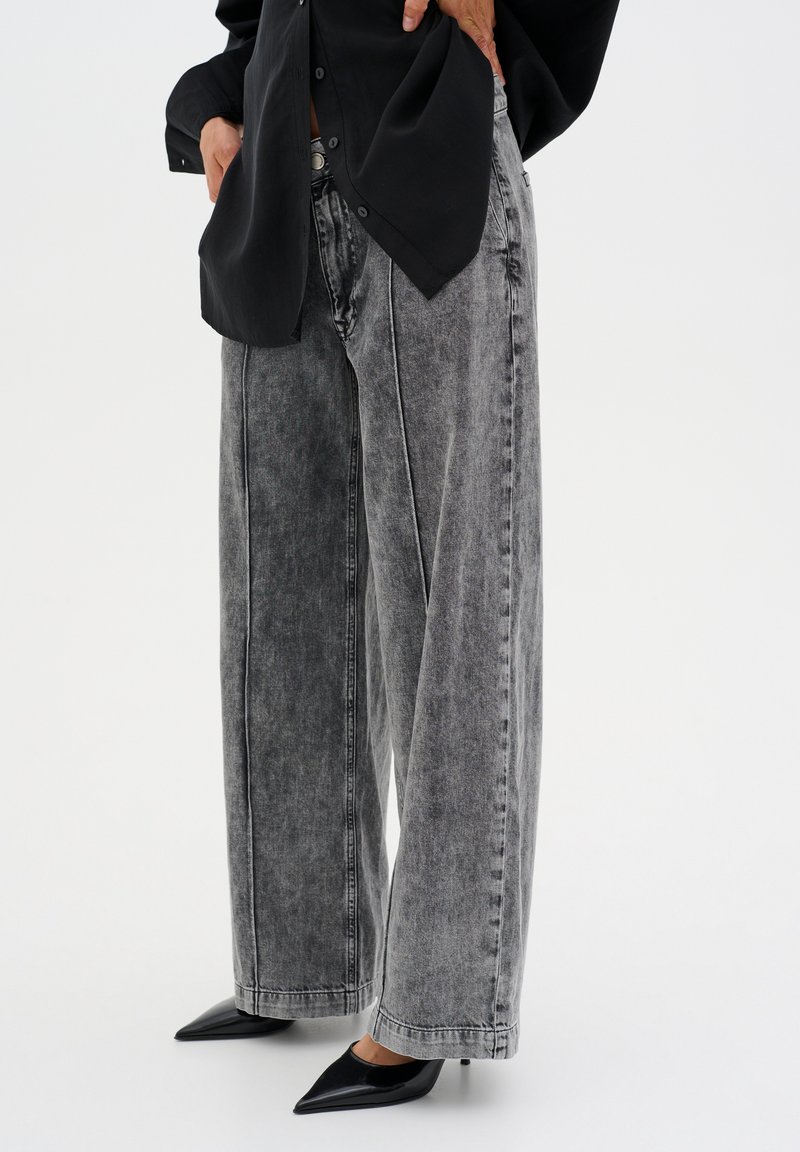 High-waisted, wide-leg gray denim jeans with a faded texture, complemented by a black blouse and pointed black heels.