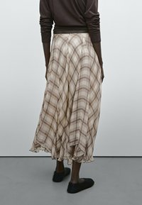 Cremefarbener Karorock aus leichtem Stoff, mit einem fließenden Design, das unterhalb der Knie fällt. Der Bund ist tailliert und plissiert.