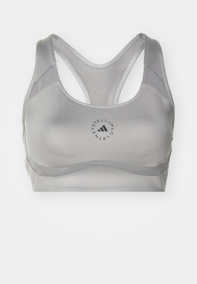 Sujetador deportivo gris con una textura suave, que presenta un diseño de espalda entrecruzada y un logo circular en el centro. Sin patrones ni acentos adicionales.