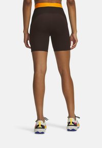 Shorts bruns taille haute et ajustés avec une ceinture orange. Portés avec des chaussures de sport multicolores présentant des accents noirs, gris, jaunes et violets.