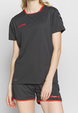 Top deportivo negro con escote y acentos rojos, con mangas cortas y logo. Combinado con pantalones cortos negros a juego con ribetes rojos.