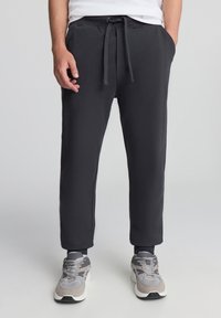 Czarne dresowe spodnie z miękkiego materiału, z elastycznym pasem w talii i sznurkiem do regulacji, kieszeniami bocznymi oraz zwężanymi mankietami.