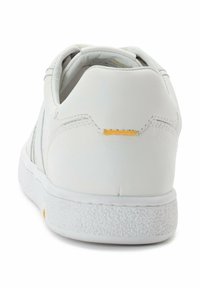 Weiße Sneaker mit einem glatten Leder-Obermaterial, einer strukturierten Gummisohle und einem kleinen gelben Akzent an der Ferse. Einfaches und minimalistisches Design.