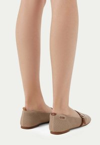 Beige tygskor med ett texturerat mönster, rund tå och ett brunt accentband. Logotypen "Gobi" på hälen. Platt suldesign.