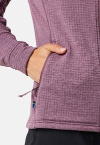 Veste zippée violette avec un motif texturé, dotée d'une poche avant et d'un ourlet ajustable. Détail accentué incluant un petit drapeau suédois.