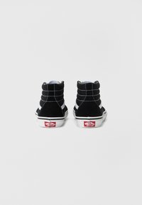 Czarne zamszowe trampki typu high-top z białymi przeszyciami i białą gumową podeszwą. Posiadają czerwone logo Vans na pięcie.