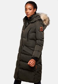 Puffer coat in dark green, featuring a faux fur hood, zippered pockets, and a logo patch on the sleeve. Soft, quilted texture.